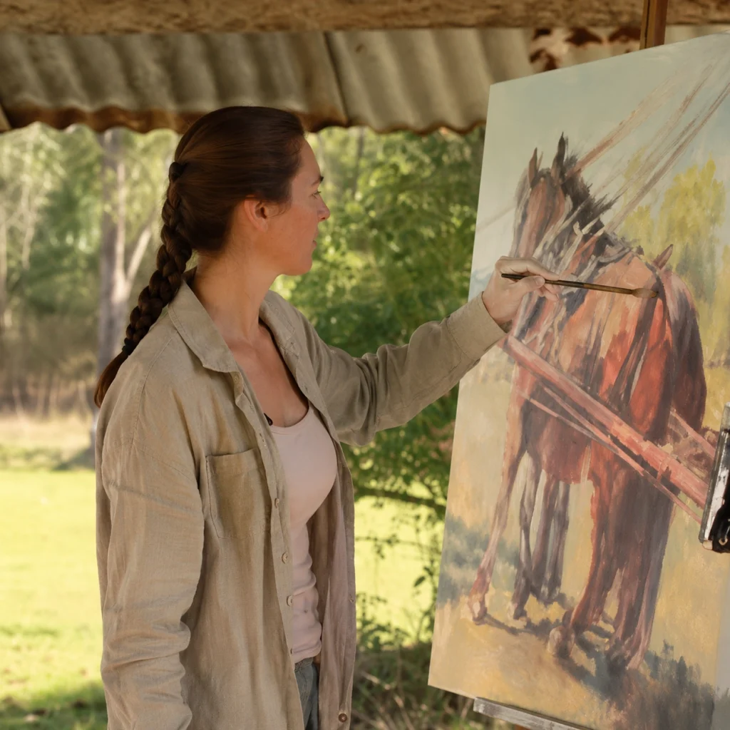 Photo of Jo S Stacey working on a new painting of a horse outside on her acreage